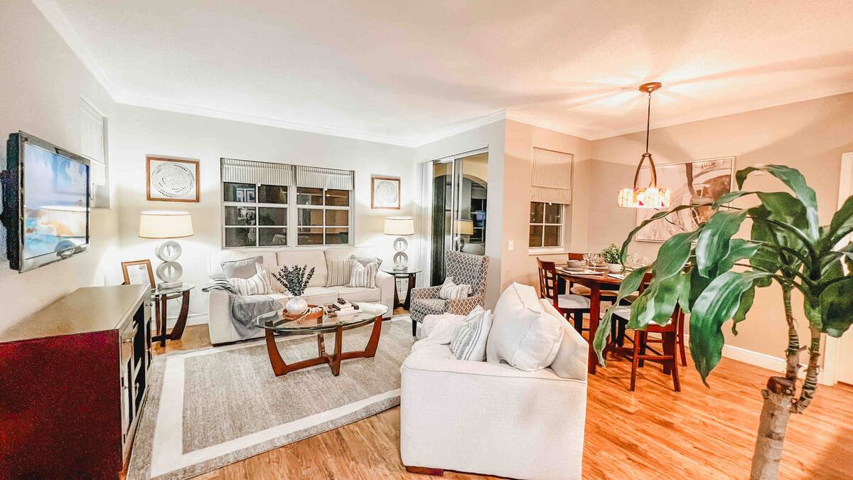 Living room of the one-bedroom apartment with white sofas, hardwood floors, and a dining area beyond