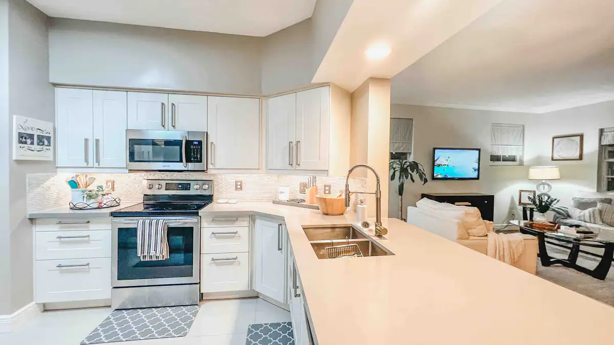 Modern kitchen with white shaker cabinets, a double sink, and a gas range opening to the living area