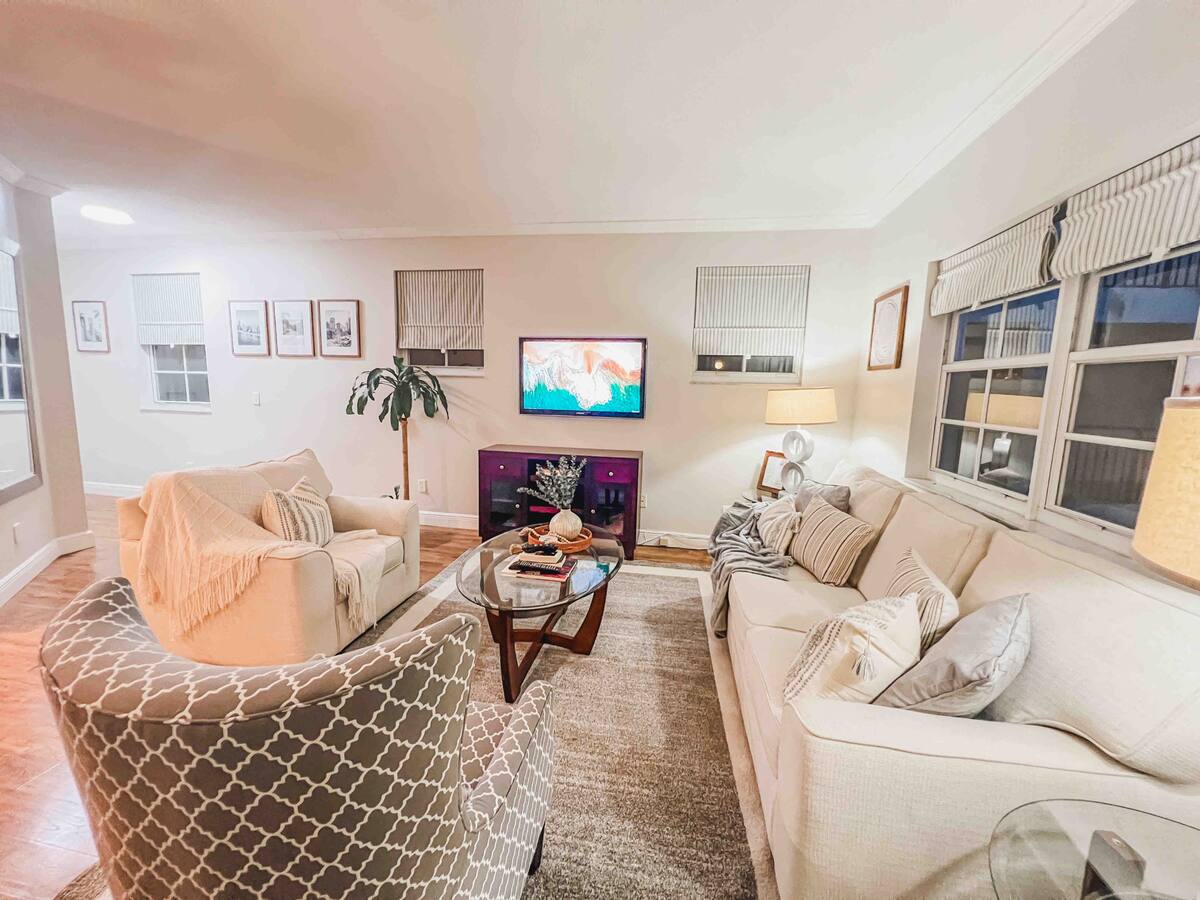 Living room with a sectional sofa, mounted TV, and a tropical palm by the window