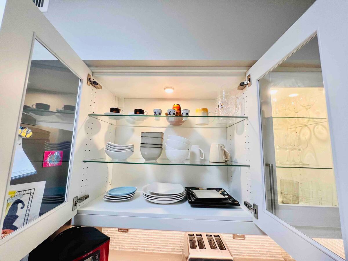 Open kitchen cabinet showing white dinnerware and serving dishes for extended-stay guests