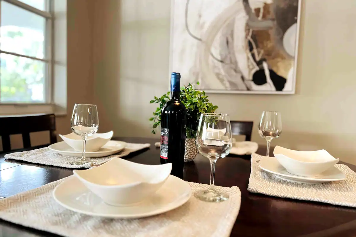 Dining table set for two with wine, eucalyptus centerpiece, and white china in the Aventura one-bedroom