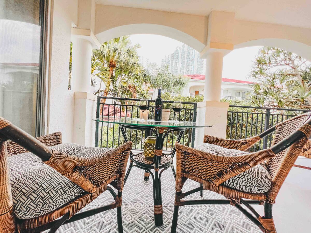Balcony seating with rattan chairs and a glass table overlooking the courtyard and palm trees