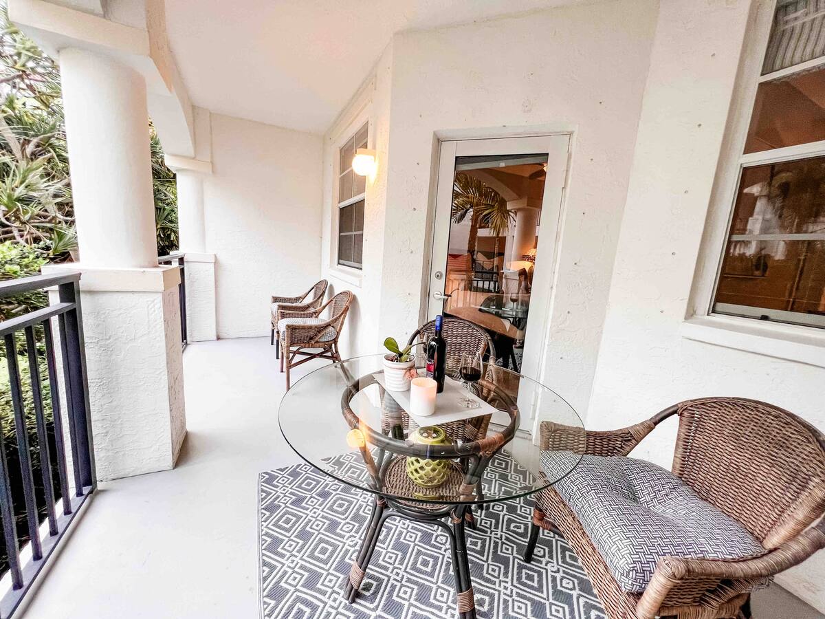 Long covered balcony with multiple wicker chairs and a glass table overlooking the courtyard at Village By The Bay
