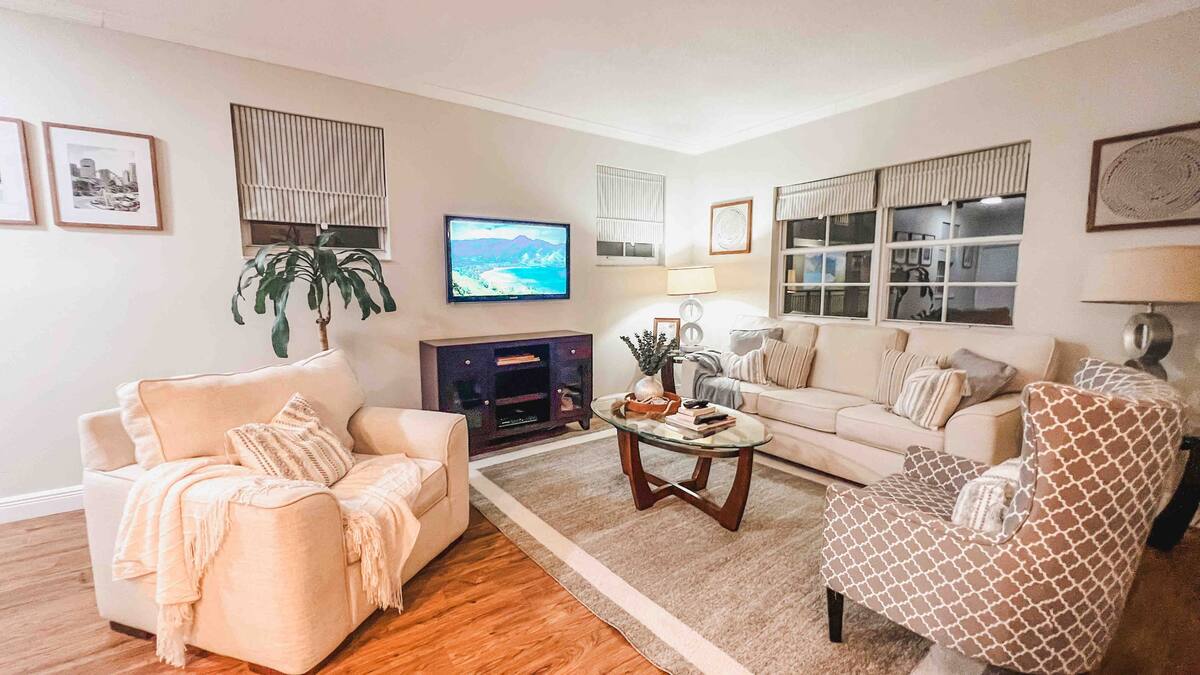 Living room with a mounted TV, cream sofas, and tropical palm decor in the Aventura one-bedroom apartment