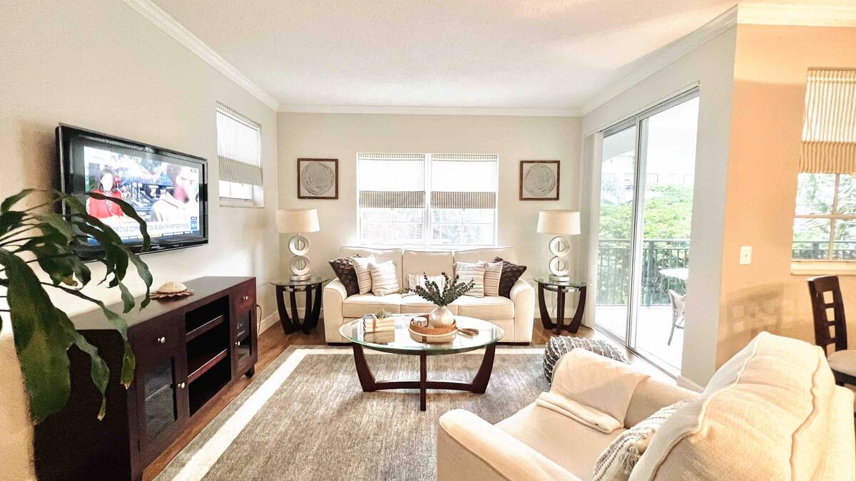 Living room with a wall-mounted TV, cream sofas, and sliding doors to the balcony in the Aventura one-bedroom rental